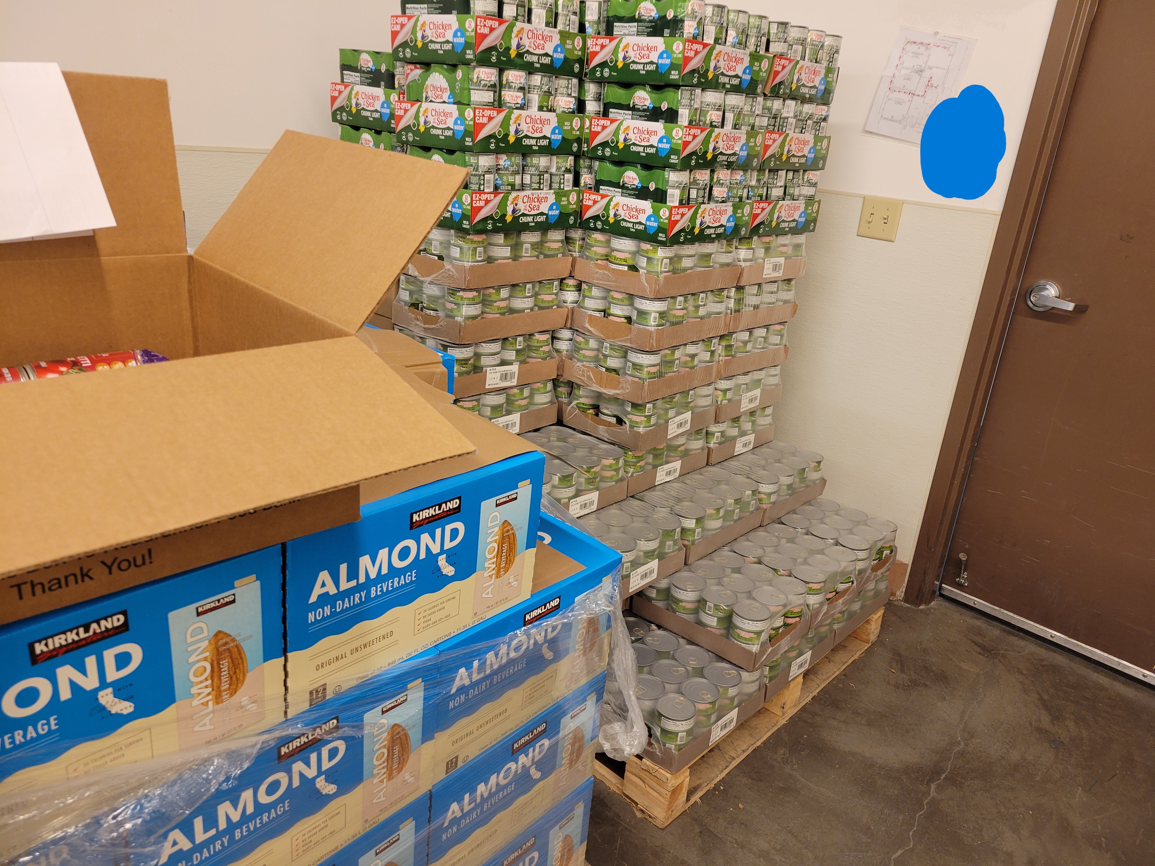 Pallets of canned tuna and boxed almond milk with a cardboard box on one.